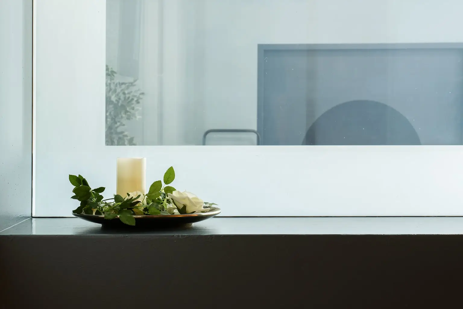 Dekorativer Teller mit weißer Kerze, Rosen und grünem Blattwerk auf einem dunklen Untergrund.