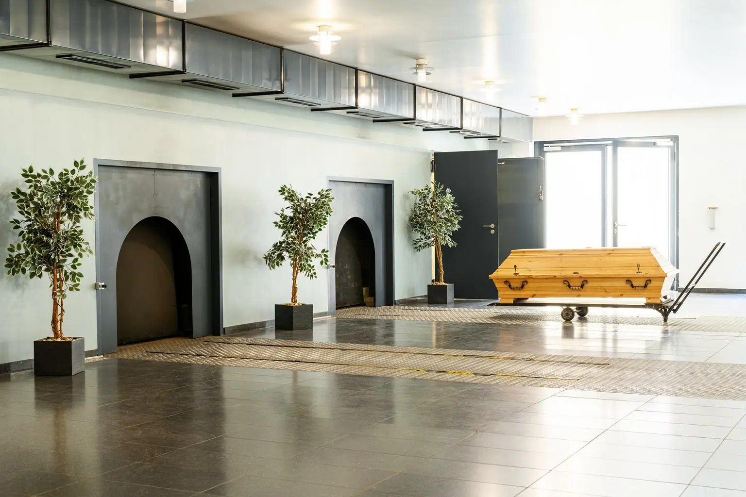 Holzsarg auf Rollwagen in einem hellen Krematorium vor den Ofennischen.