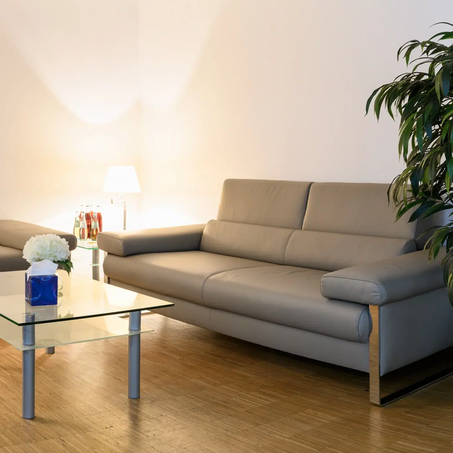 Heller Abschiedsraum mit Sofa, Glastisch, Blumen und Taschentüchern.