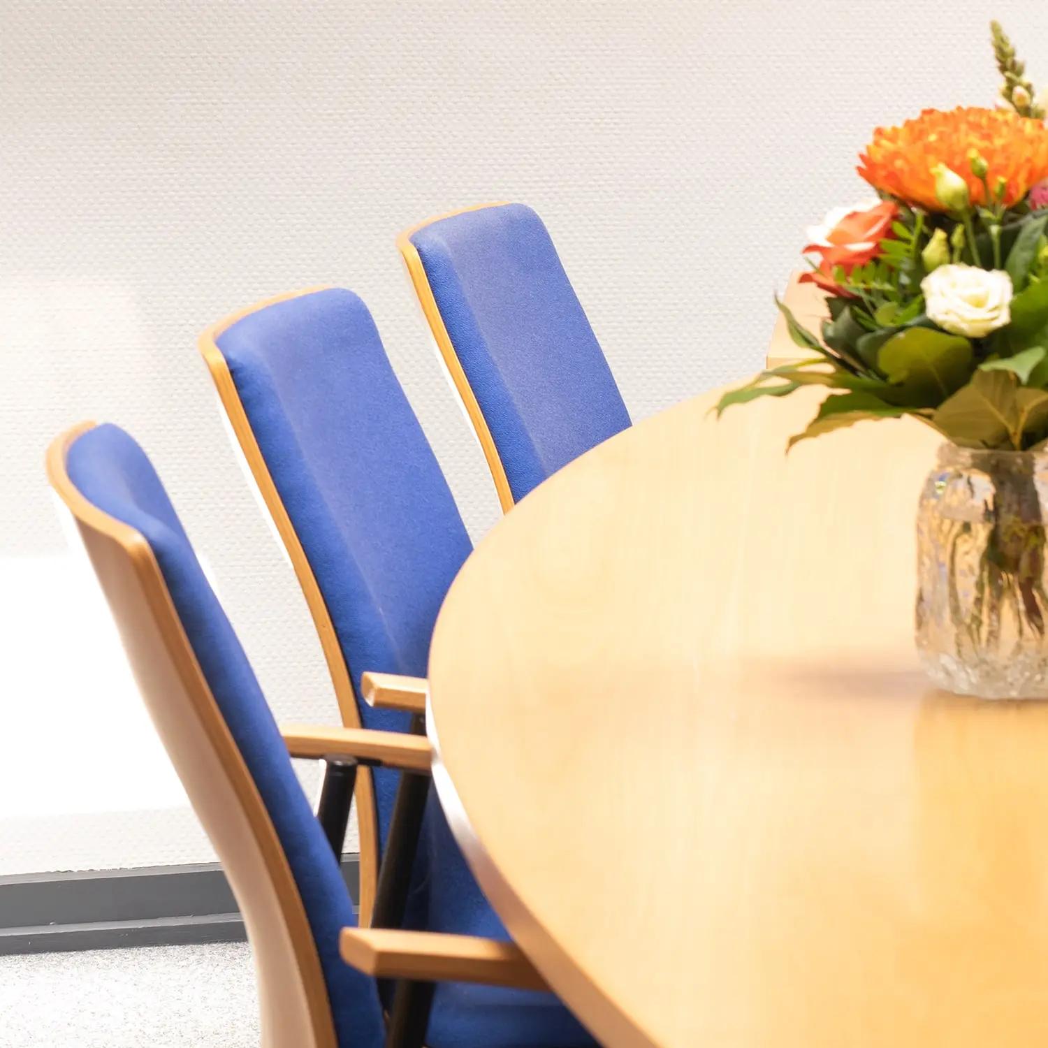 Runder Konferenztisch mit blauen Stühlen und Blumenstrauß